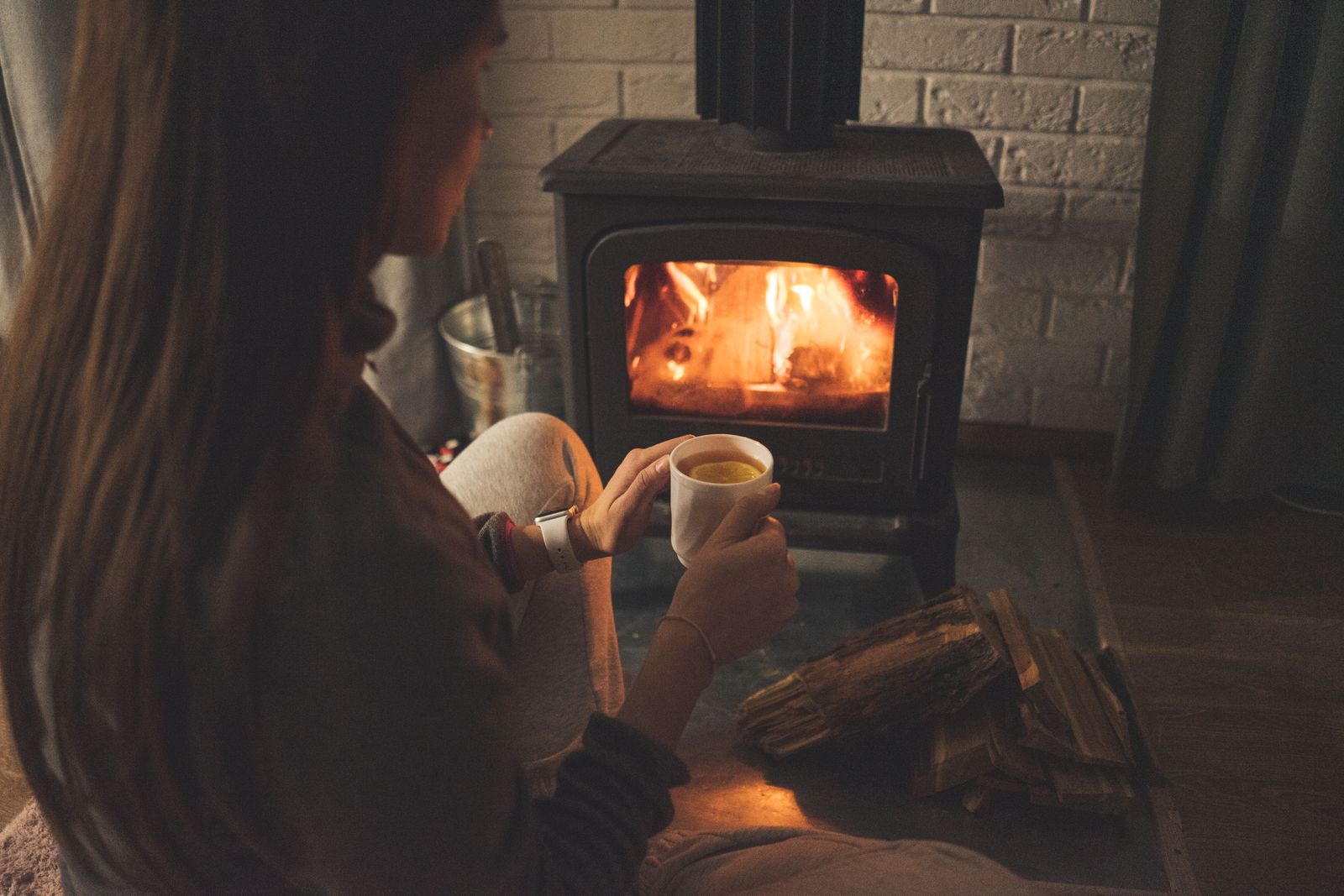 Someone enjoying tea beside a glowing wood stove